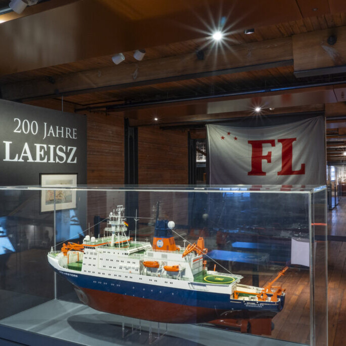 Modell eines Forschungsschiffs in einer Glasvitrine in einem holzgetäfelten Museumsraum, links die Aufschrift 200 Jahre F. Laeisz und im Hintergrund ein großes Banner mit roten Buchstaben FL.