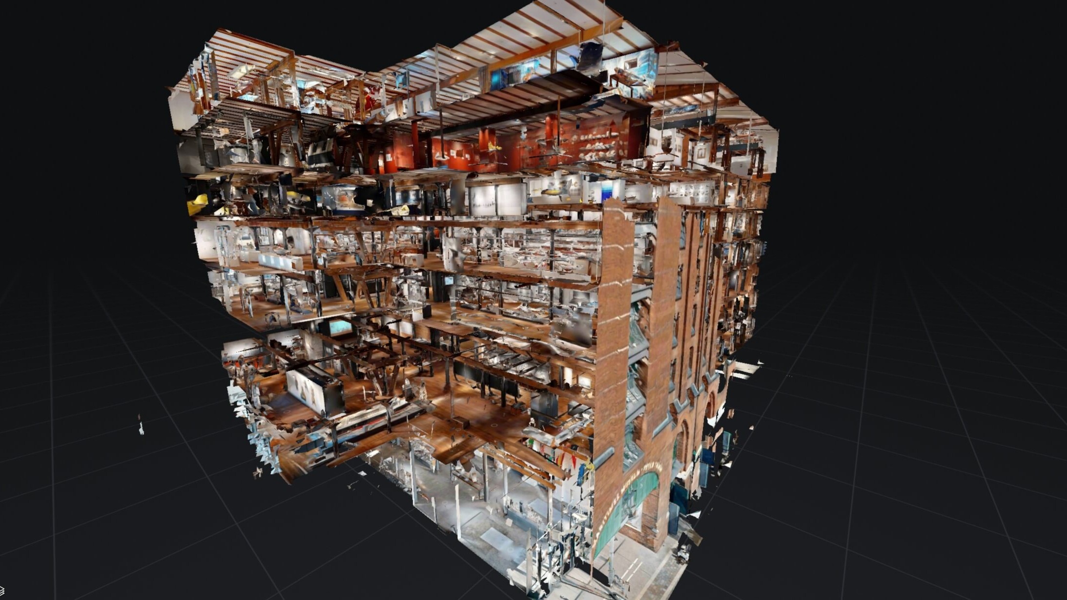 Aufgeschnittenes 3D‑Dollhouse-Modell eines mehrgeschossigen Gebäudes, das freigelegte Etagen, Räume, Treppen, Möbel und eine Backsteinfassade mit Bogenportal vor dunklem Rasterhintergrund zeigt.