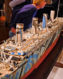 Detailliertes Schiffsmodell mit vier Schornsteinen, zahlreichen Rettungsbooten und auffälliger Dazzle‑Tarnung in Blau, Grau und Rot im Museum.