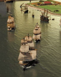 Diorama mit mehreren historischen Dreimast-Segelschiffen in Formation auf ruhigem Wasser, mit Booten und einer grünen Küstenlandschaft im Hintergrund.