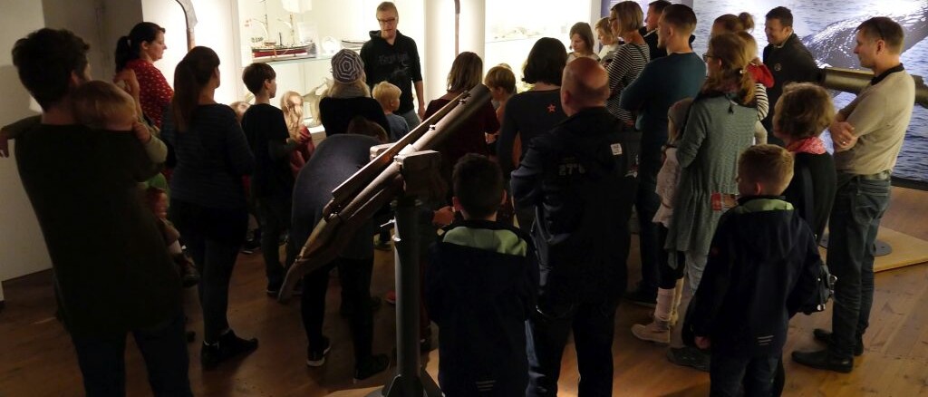 Gruppe von Erwachsenen und Kindern bei einer Museumsführung vor Vitrinen mit Schiffsmodellen