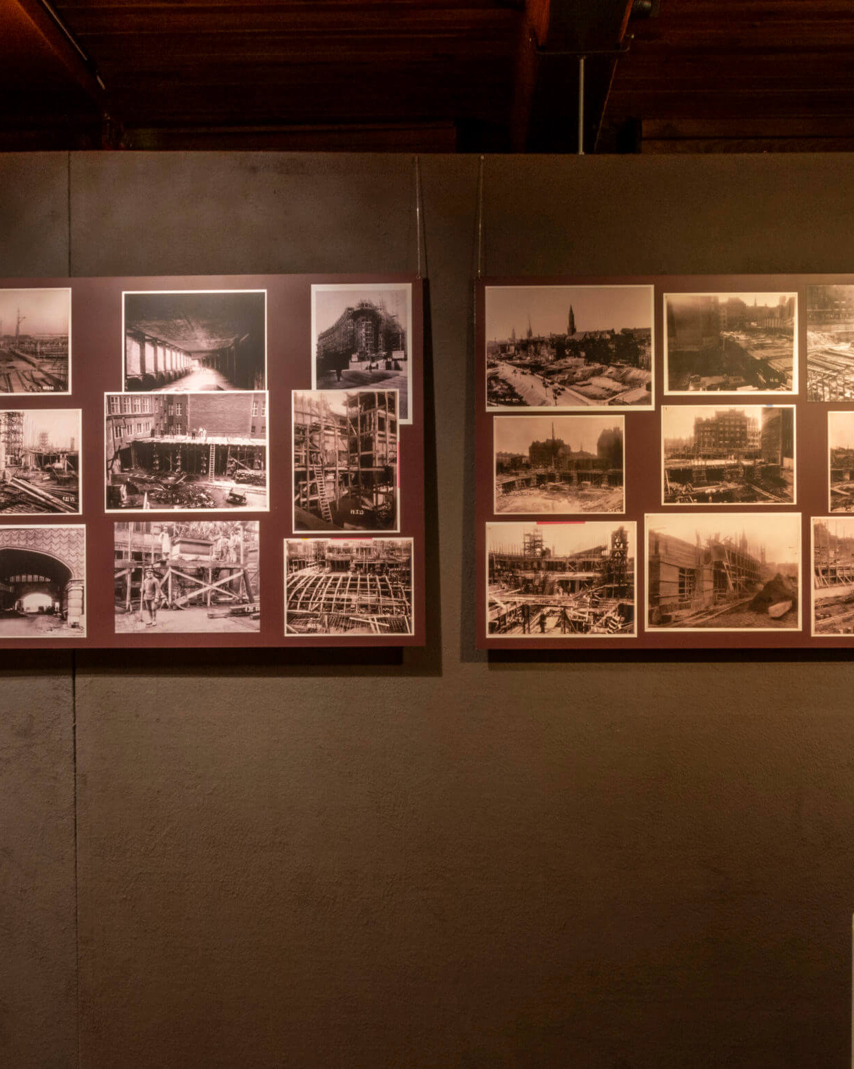 Museumswand mit drei dunkelroten Informationstafeln – zwei schmale Textfelder links und rechts und in der Mitte zwei große Tafeln mit mehreren historischen Sepia-/Schwarzweiß-Fotografien und erklärendem Text über das Bauprojekt „Schiff aus Stein“, rechts unten eine Glasvitrine sichtbar.