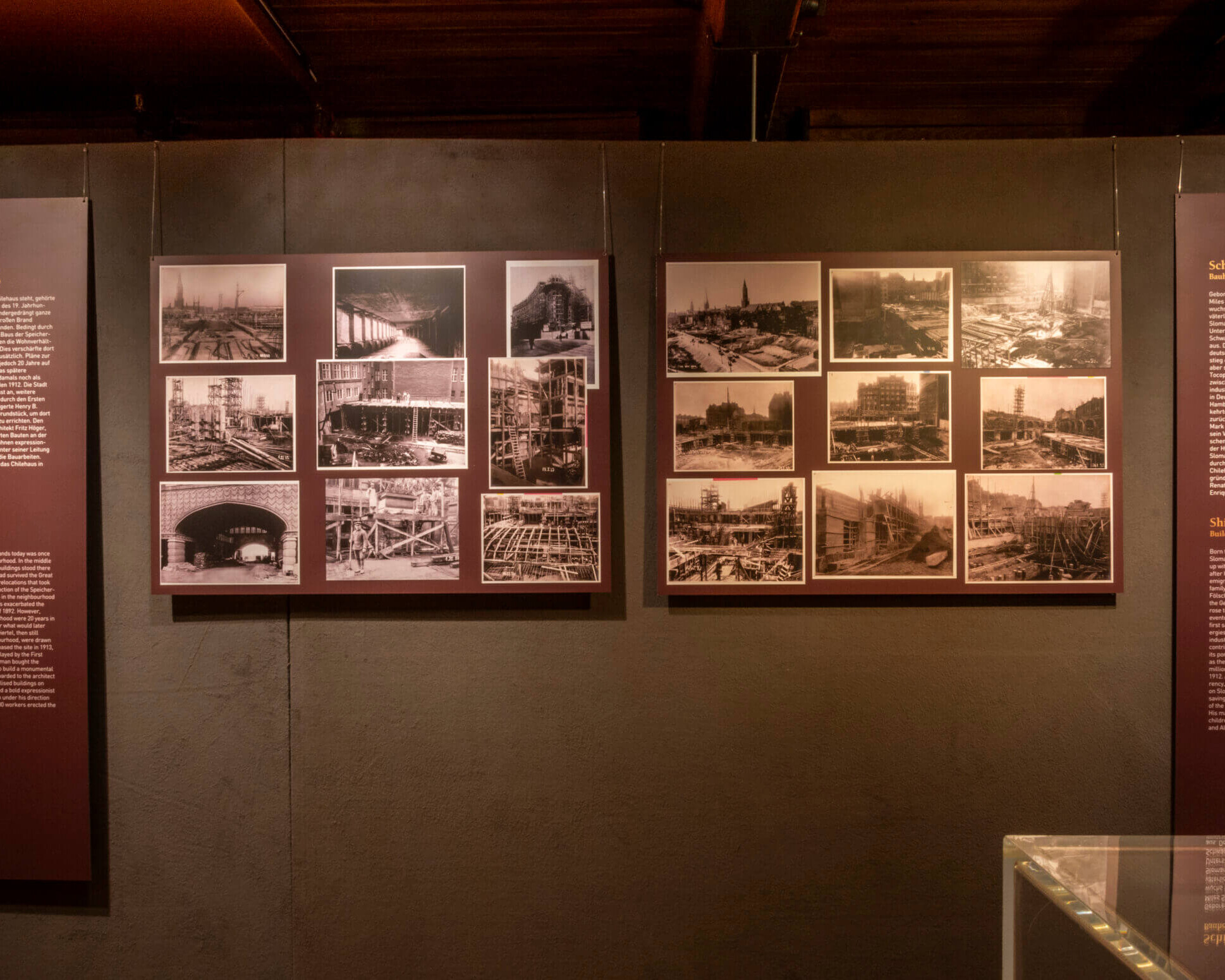 Museumswand mit drei dunkelroten Informationstafeln – zwei schmale Textfelder links und rechts und in der Mitte zwei große Tafeln mit mehreren historischen Sepia-/Schwarzweiß-Fotografien und erklärendem Text über das Bauprojekt „Schiff aus Stein“, rechts unten eine Glasvitrine sichtbar.