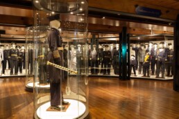 Museumsraum mit Mannequins in Militär- und Marineuniformen; im Vordergrund ein Offiziersmannequin in rundem Glaskolben mit goldverziertem Degen.