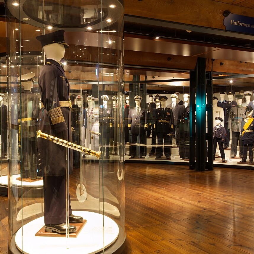 Museumsraum mit Mannequins in Militär- und Marineuniformen; im Vordergrund ein Offiziersmannequin in rundem Glaskolben mit goldverziertem Degen.
