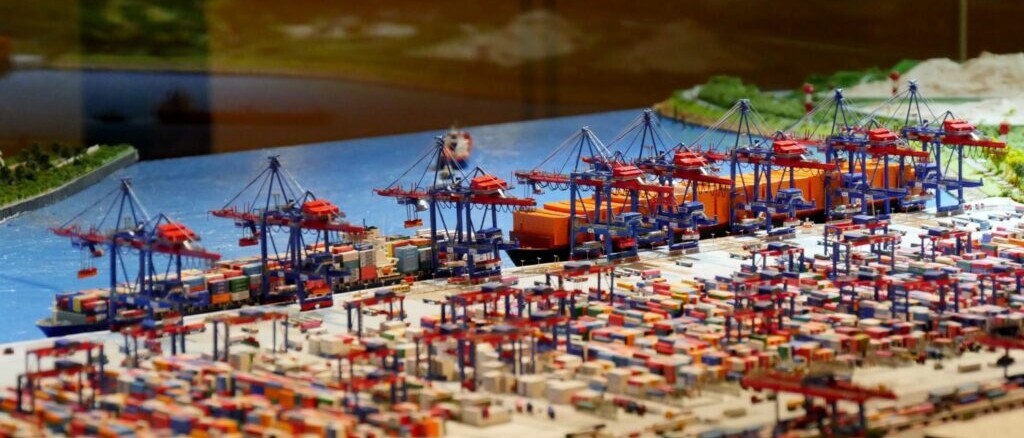 Miniaturmodell eines Containerhafens mit zahlreichen Kränen, Containerschiffen und dicht gestapelten Containern am Kai.