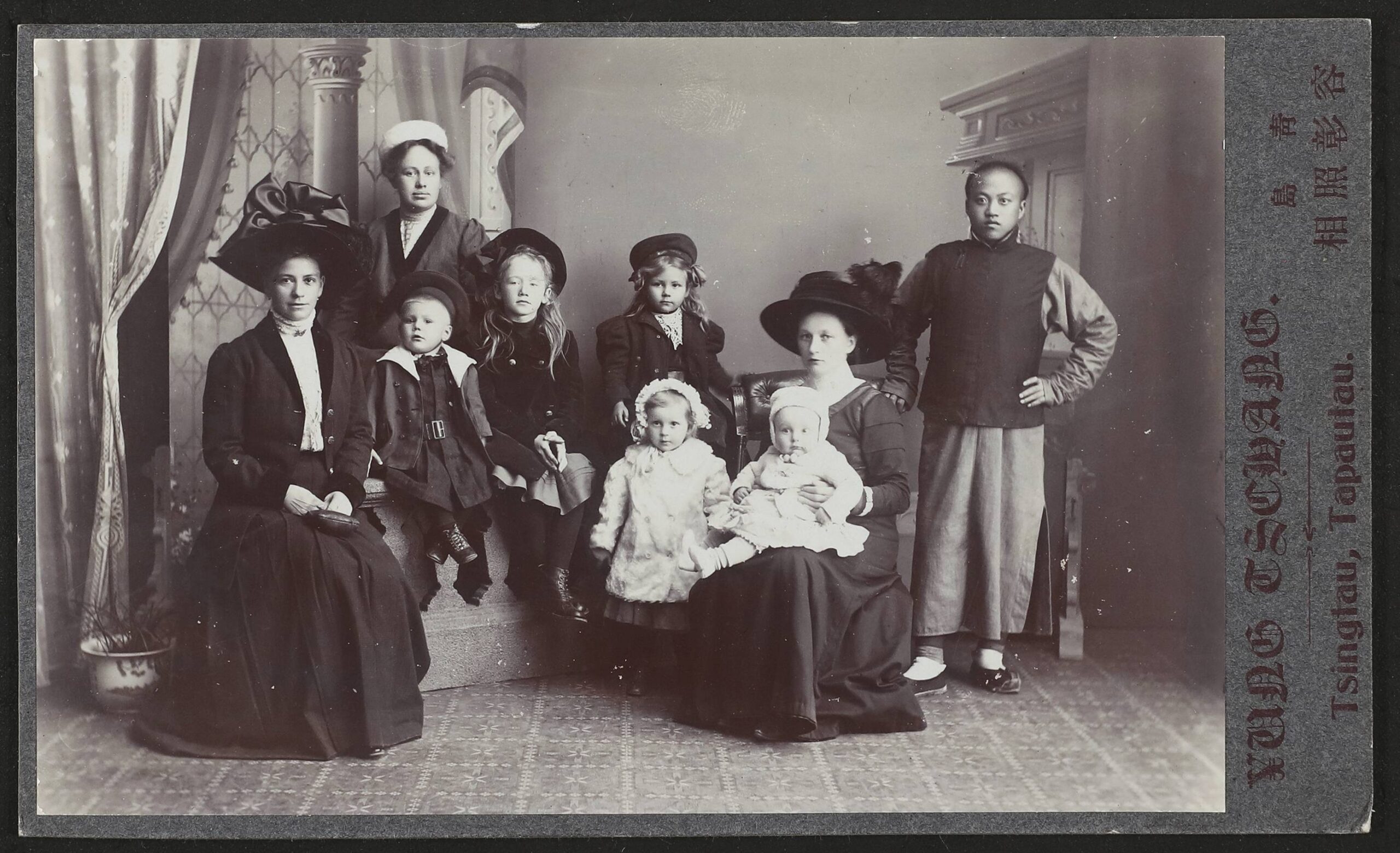 Neun Personen in einem Studio-Portr&auml;t: Frauen und Kinder in historischer Kleidung mit gro&szlig;en H&uuml;ten, rechts ein Mann in dunkler Jacke und weitem Rock.