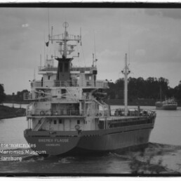 Frachtschiff Bremer Flagge (Hamburg) fährt auf einem Kanal, schwarzweißaufnahme, zweites Schiff im Hintergrund und Uferbäume.