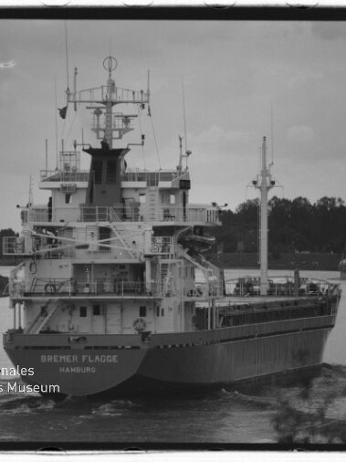 Frachtschiff Bremer Flagge (Hamburg) fährt auf einem Kanal, schwarzweißaufnahme, zweites Schiff im Hintergrund und Uferbäume.