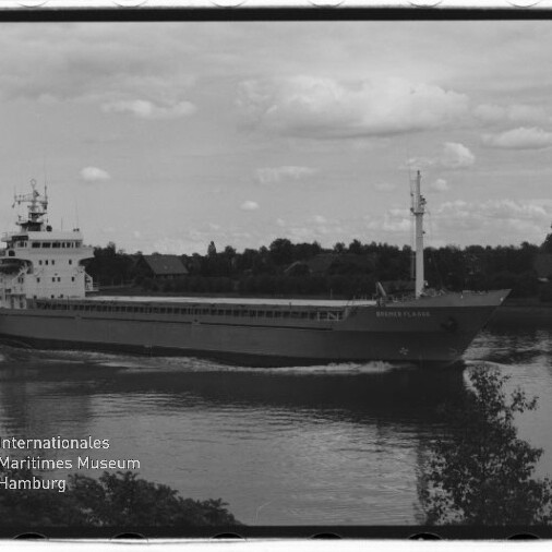 Schwarzweißfoto eines Frachtschiffs auf ruhigem Fluss vor baumbewachsenem Ufer; Wasserzeichen Maritimes Museum Hamburg