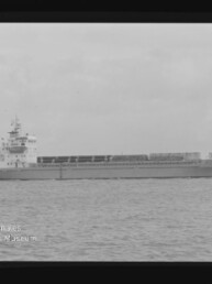 Seitliche Aufnahme eines Frachtschiffs auf ruhiger See in Schwarzweiß mit Filmrand und Museumslogo.