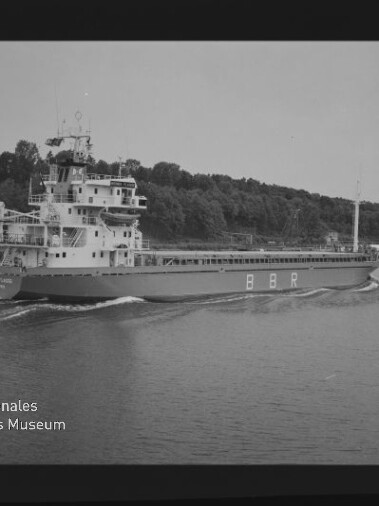 Frachtschiff mit großen Aufbauten und Schriftzug BBR fährt auf einem Fluss, bewaldetes Ufer im Hintergrund.