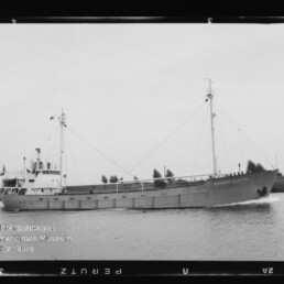 Frachtschiff mit zwei Masten und achterlicher Brücke fährt auf ruhigem Kanal vor baumbesetztem Ufer; Museumslogo unten links.