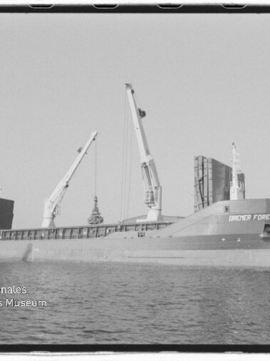 Frachtschiff BREMER FOREST am Kai mit Ladekränen im Hafen, Wasser im Vordergrund und Museumsstempel links unten.