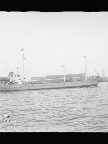 Frachtschiff im Hafen vor Kaimauer und Hafenkränen, Wellen im Vordergrund und Museum-Logo unten links.
