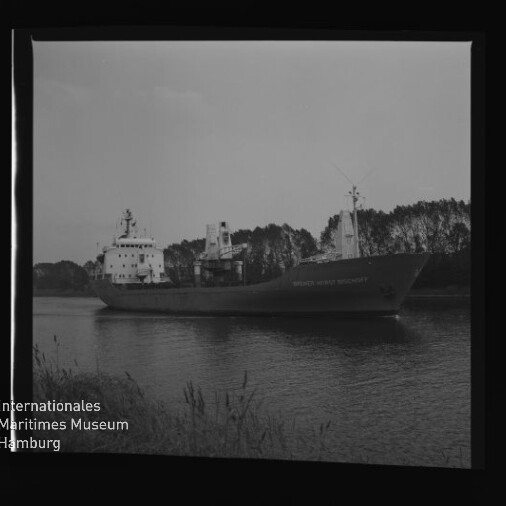 Frachtschiff auf ruhigem Kanal vor einer Baumreihe; links unten Logo und Schriftzug Internationales Maritimes Museum Hamburg.