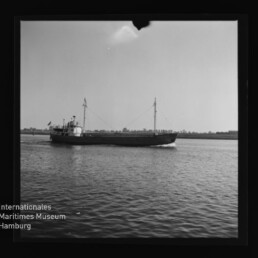 Kleiner Frachter auf ruhigem Wasser in Schwarzweiß; unten links Schriftzug Internationales Maritimes Museum Hamburg.