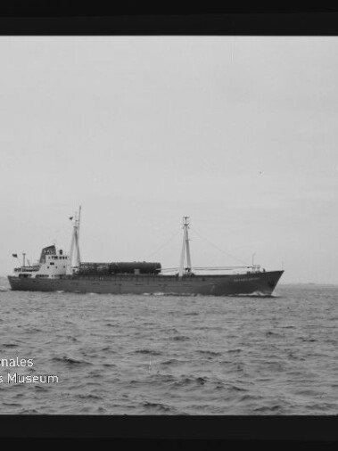 Frachtschiff in Seitenansicht mit Mast und Heckaufbau auf ruhiger See; links unten Museum-Logo.
