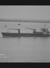 Frachtschiff mit zwei Kranen und Schriftzug BBR auf ruhigem Wasser vor Küste; Museumslogo unten links