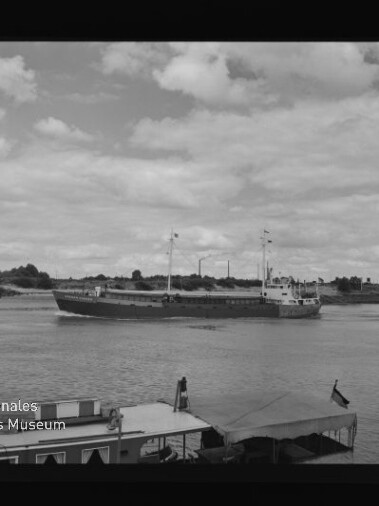 Frachtschiff auf Fluss vor flachem Ufer; im Vordergrund Boote und der Schriftzug Internationales Maritimes Museum Hamburg