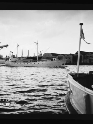 Schwarzweiß-Hafenbild: großes Schiff mittig, kleines Boot mit Flagge vorn, Werft hinten, Wasserzeichen Maritimes Museum