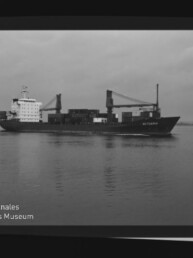 Schwarzweißaufnahme eines Frachtschiffs mit Deckskranen und Containern auf ruhigem Meer, Filmrand mit AGFA PAN 100 und Museumswasserzeichen.