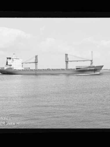 Frachtschiff mit zwei Ladekränen fährt auf ruhiger See, schwarz-weiße Aufnahme mit sichtbarem Filmrand.