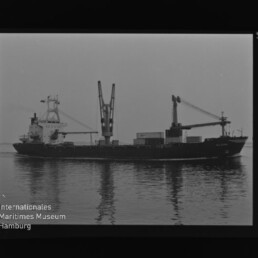 Frachtschiff mit Deckskränen und Containern auf ruhigem Wasser, Spiegelung; Schriftzug Internationales Maritimes Museum Hamburg