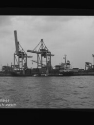 Hafen mit großen Containerkränen, angedocktem Frachtschiff, Wasser vorne und Wasserzeichen des Maritimen Museums Hamburg.