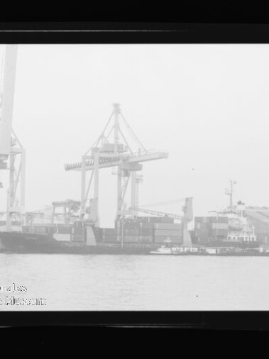 Frachtschiff unter großen Hafenkränen an der Kaimauer, kleines Schleppboot davor; Rahmen mit Maritimes Museum Hamburg.