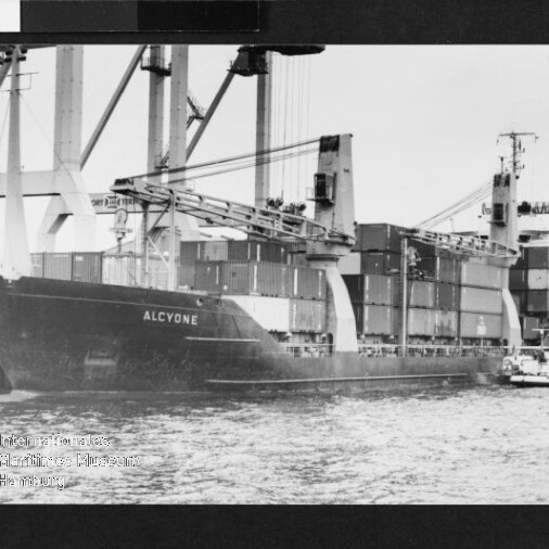 Containerschiff ALCYONE am Hafen mit großen Verladekränen, gestapelten Containern und einem kleinen Schlepper.