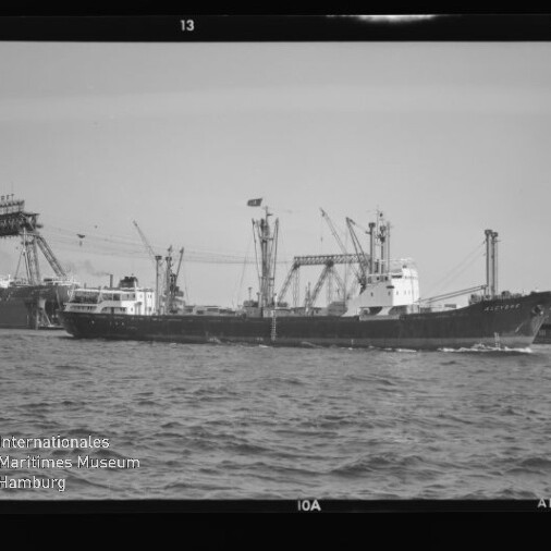 Frachtschiff fährt am Hafen vorbei, im Hintergrund Kräne und Werft, Wasser im Vordergrund und Museumssignet unten links.