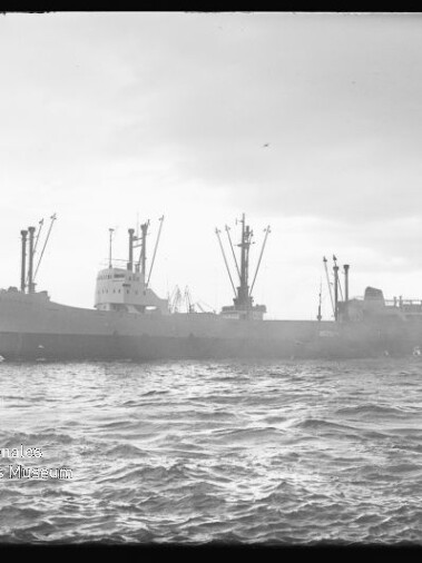 Frachtschiff mit mehreren Ladekränen vor Hafen bei welliger See, Wasserzeichen des Internationalen Maritimen Museums Hamburg.