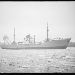 Frachtschiff in Seitenansicht auf zugefrorenem Wasser vor Hafenanlagen, kleines Museum-Logo links unten.