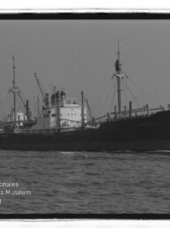 Frachtschiff mit mehreren Masten und rauchendem Schornstein im Hafen; Wasserzeichen Internationales Maritimes Museum Hamburg unten links.