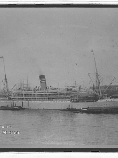 Passagierdampfschiff mit hohem Schornstein und Masten im Hafen, umgeben von kleinen Booten, historische Schwarzweißaufnahme.