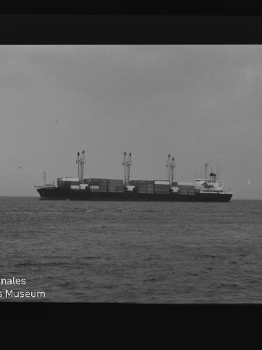 Frachtschiff mit Kränen und Containerstapeln auf ruhiger See, schwarzweißaufnahme mit Museumslogo unten links