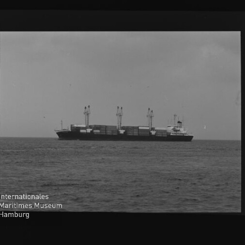 Frachtschiff mit Kränen und Containerstapeln auf ruhiger See, schwarzweißaufnahme mit Museumslogo unten links
