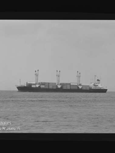 Containerschiff mit Ladekränen auf ruhiger See, mittig im Bild, umrahmt von Filmrand mit AGFA-Schrift und Museumssiegel.