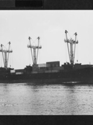 Schwarzweißfoto eines Frachtschiffs mit drei Ladekränen und Containern auf ruhigem Wasser, Museumsstempel unten links.