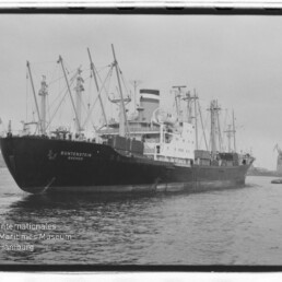 Großes Frachtschiff BUNTENSTEIN mit mehreren Ladekränen im Hafen und kleinem Lotsenboot am Heck.