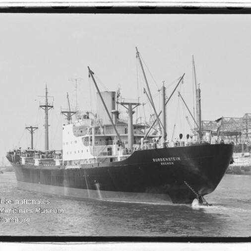 Schwarzweiß‑Frachter mit Ladekränen im Hafen, Name am Bug sichtbar und Museumswasserzeichen links unten.