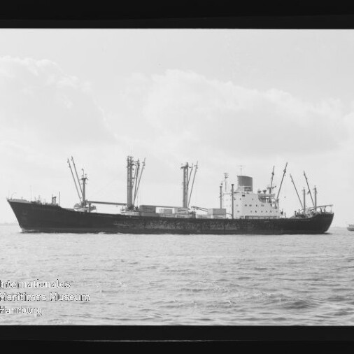 Schwarzweißfoto eines Frachtschiffs mit mehreren Ladekränen auf ruhiger See, Museumslogo unten links.