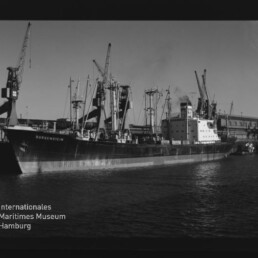 Frachtschiff Bungenstein im Hafen vor Ladekränen, Schwarzweißaufnahme mit Museumslogo
