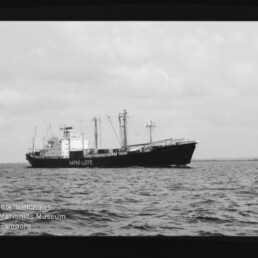 Schwarzweiß-Aufnahme eines Hapag‑Lloyd Frachtschiffs auf ruhiger See unter bewölktem Himmel, Museumswasserzeichen links unten.