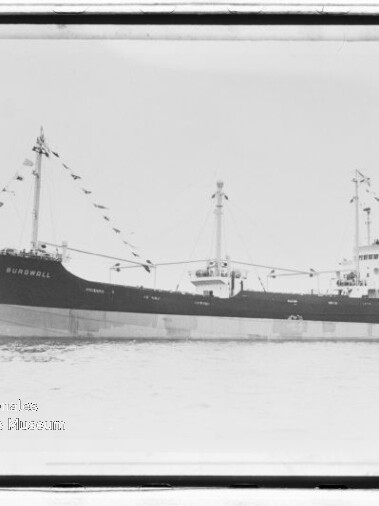 Schwarzweiß-Seitenansicht eines angeflagten Frachtschiffs, das auf ruhigem Wasser fährt.