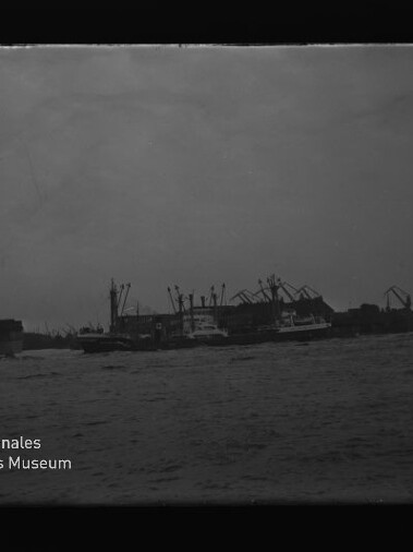 Hafen mit Kränen und Schiffen, Wasser im Vordergrund; Logo des Internationalen Maritimen Museums Hamburg links unten.