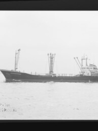 Schwarzweißfoto eines Frachtschiffs mit mehreren Ladekränen auf ruhiger See, kleines Boot am rechten Bildrand.