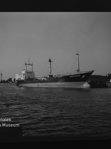 Frachtschiff mit zwei Masten im Hafen, Wasser im Vordergrund und Museum-Logo Internationales Maritimes Museum Hamburg unten links