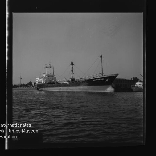 Frachtschiff mit zwei Masten im Hafen, Wasser im Vordergrund und Museum-Logo Internationales Maritimes Museum Hamburg unten links